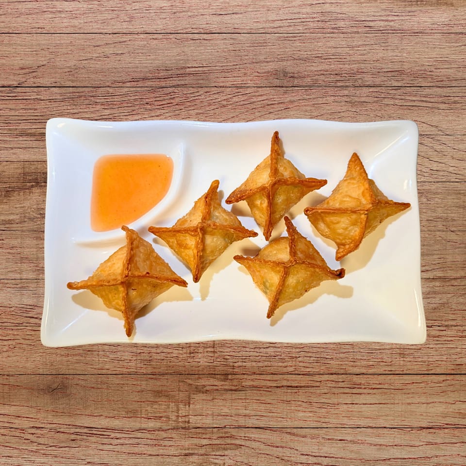 Five golden-brown crab rangoons and a small dish of orange dipping sauce on a white rectangular plate.