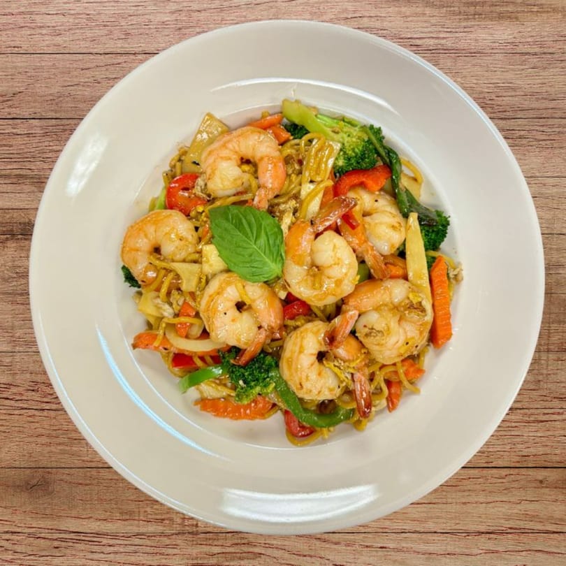 Shrimp Pad See Ew with broccoli, carrots, bell peppers, and a basil leaf on a white plate.