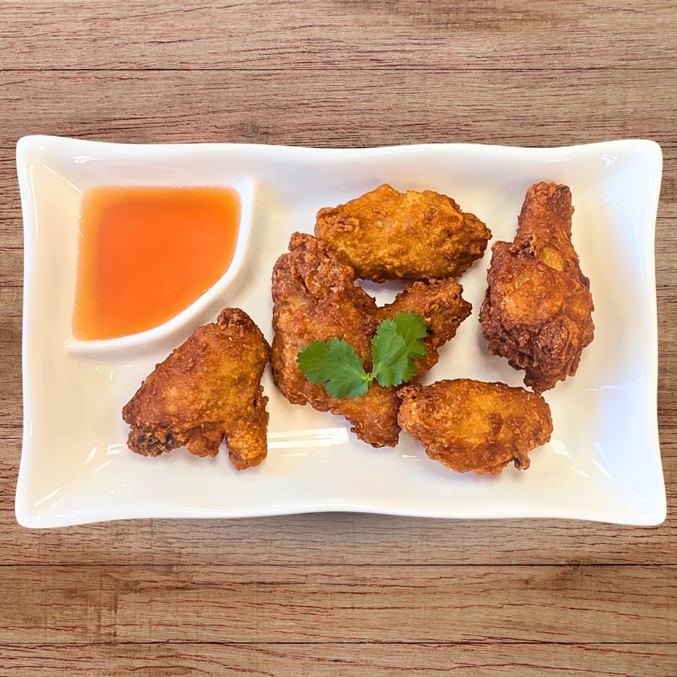 Crispy fried chicken wings with sweet chili dipping sauce and a cilantro garnish on a white plate.
