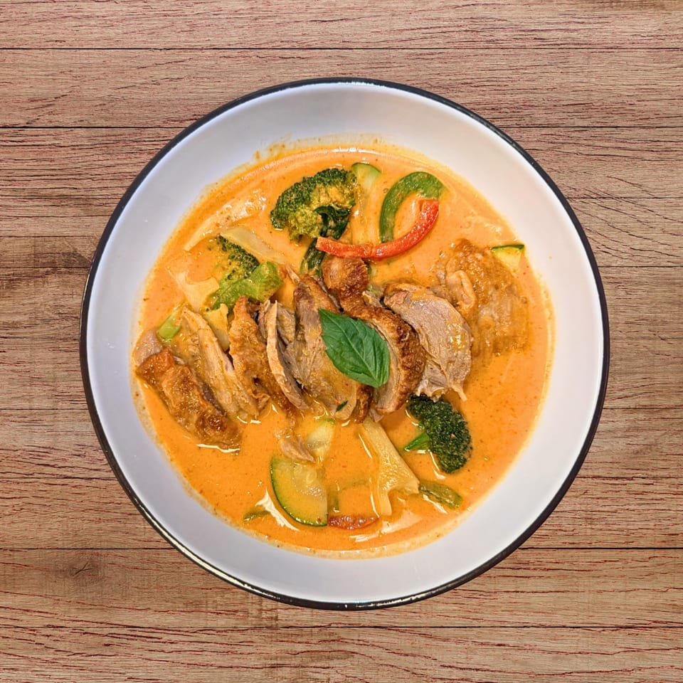 Red curry with sliced duck, broccoli, zucchini, and red peppers, garnished with basil.