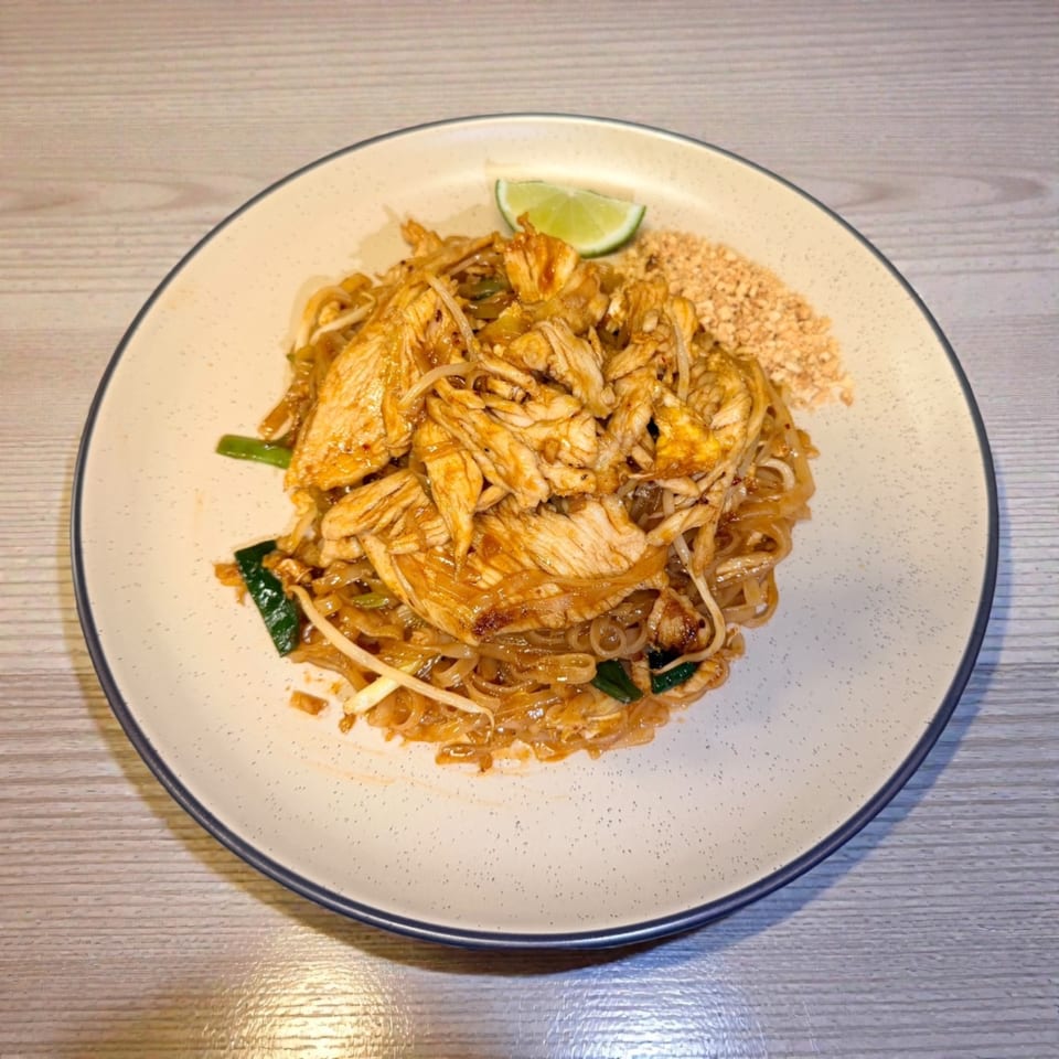 Chicken Pad Thai with noodles, bean sprouts, green onions, crushed peanuts, and a lime wedge.