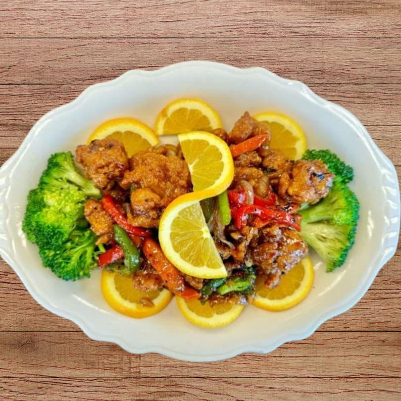 Orange chicken with broccoli and bell peppers, garnished with orange slices on a white platter.