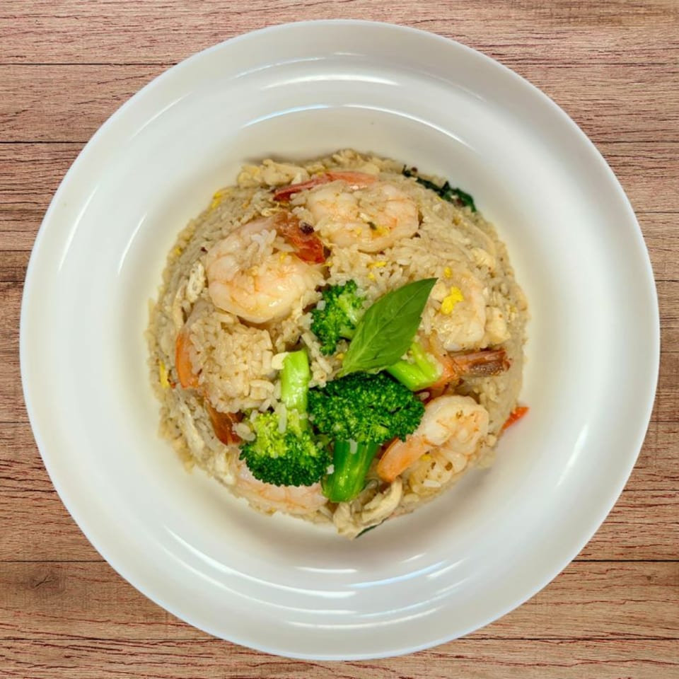 Shrimp fried rice with broccoli florets and a basil leaf, served in a white bowl on a wooden table.