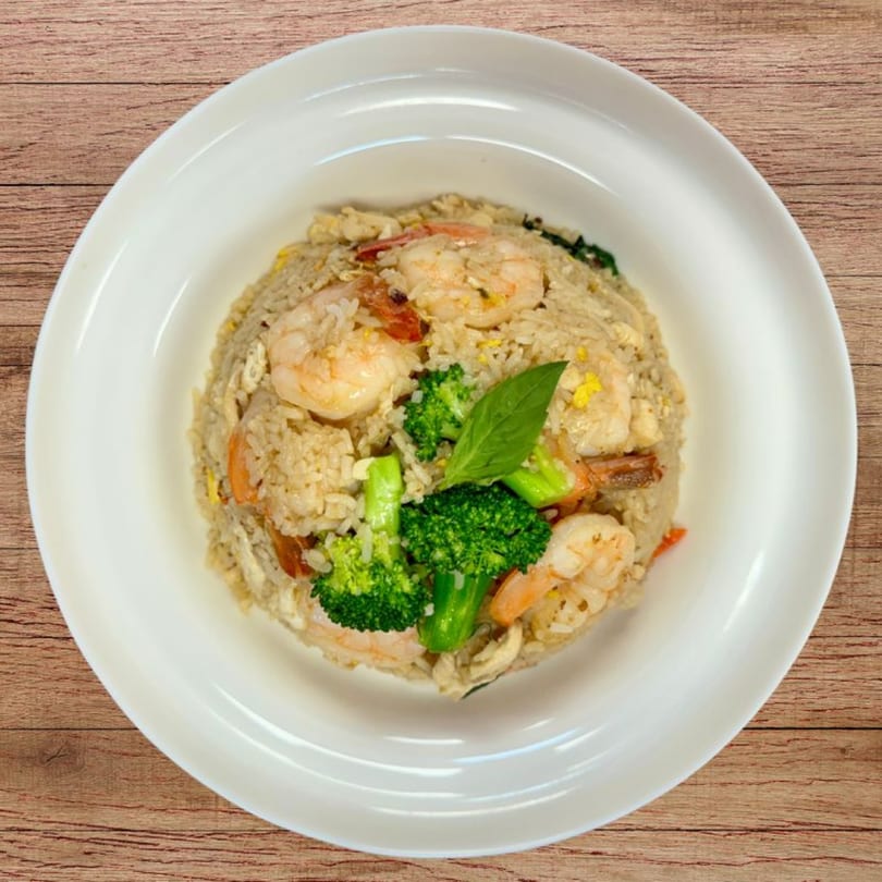 Shrimp fried rice with broccoli florets and a basil leaf, served in a white bowl on a wooden table.