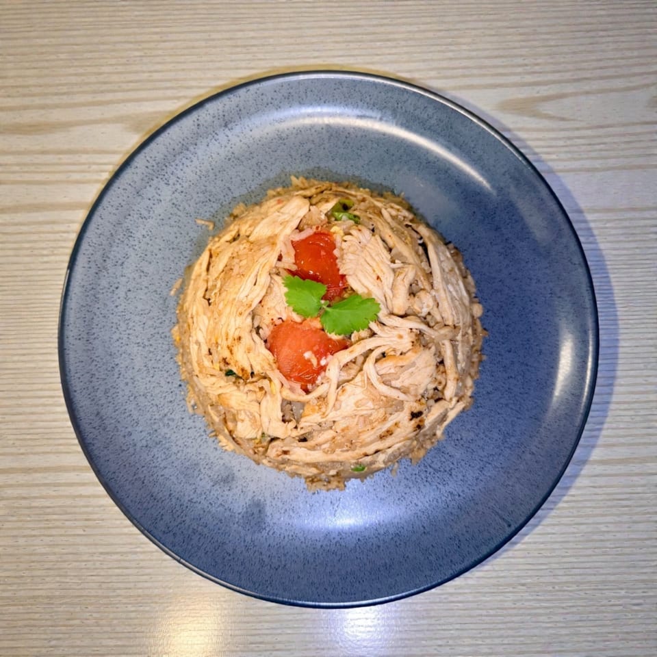 Shredded chicken and rice dish, garnished with red tomatoes and green herbs on a blue plate.