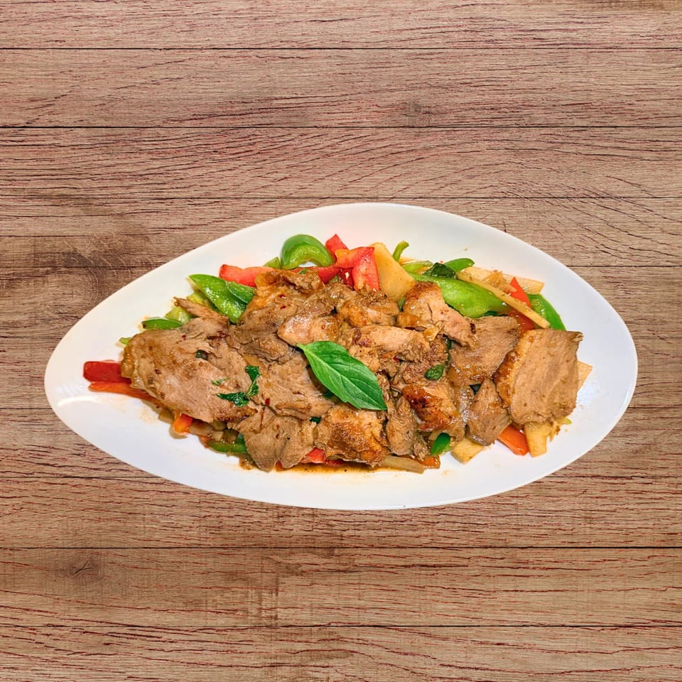 Stir-fried beef with green and red bell peppers, bamboo shoots, and basil on a white plate.