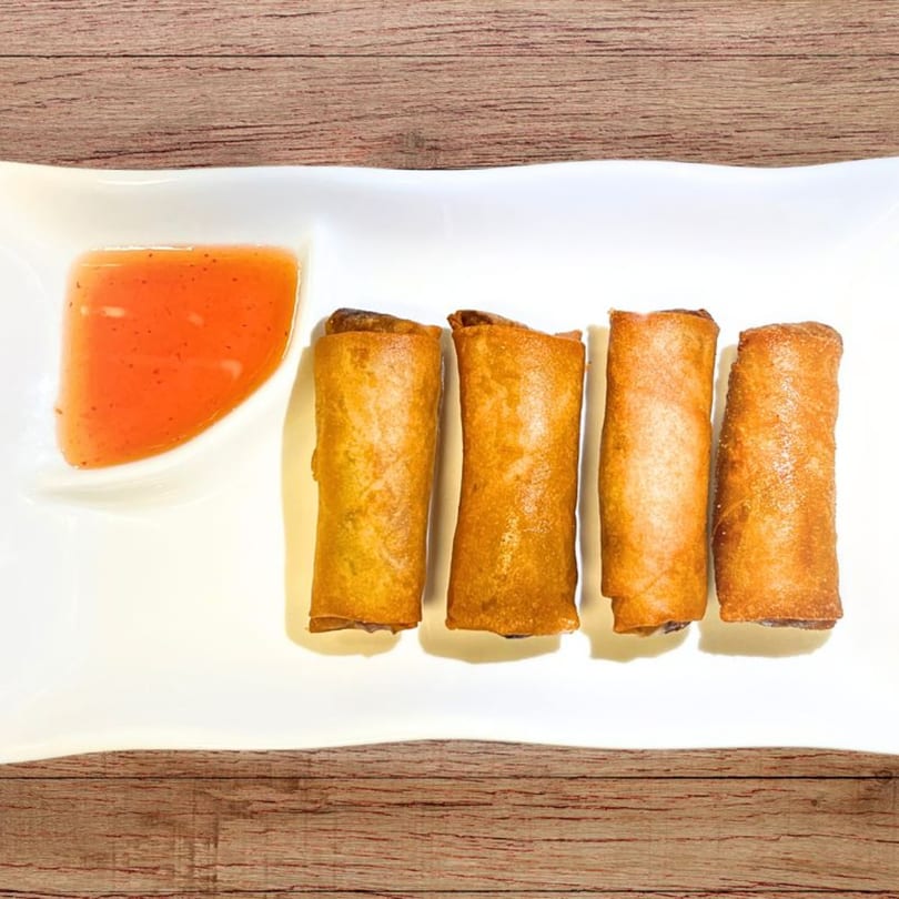 Four crispy spring rolls and a small dish of orange dipping sauce on a white plate.