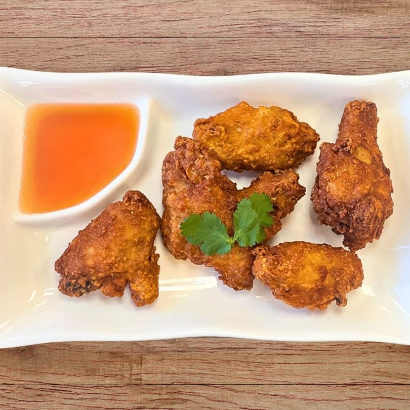 Crispy fried chicken wings with a side of orange sweet chili dipping sauce and cilantro garnish.